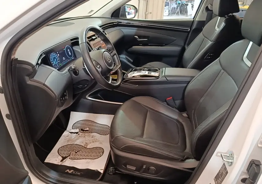 Vue intérieure côté conducteur du Hyundai Tucson blanc 2022, sièges cuir noirs et tableau de bord digital lumineux.