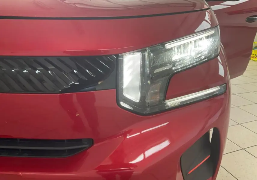 Gros plan sur l'avant droit rouge métallisé du Citroën C3 ë-113 Berline Max 2025, mettant en valeur son phare LED distinctif.