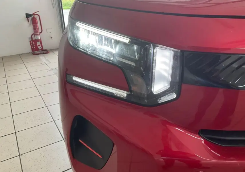 Gros plan sur l'avant gauche de la Citroën C3 ë-113 Berline Max 2025 en rouge métal foncé avec phares LED allumés.