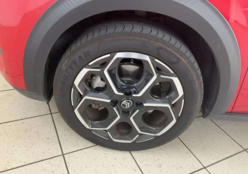 Gros plan sur la roue avant gauche d'une Citroën C3 ë-113 Berline Max 2025 rouge métal foncé avec jante noire et argent.