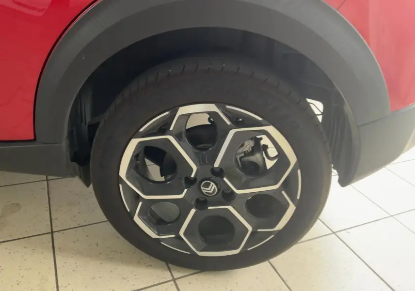 Gros plan sur la roue avant droite d'une Citroën C3 ë-113 Berline Max rouge métal foncé avec jante noire et argentée.