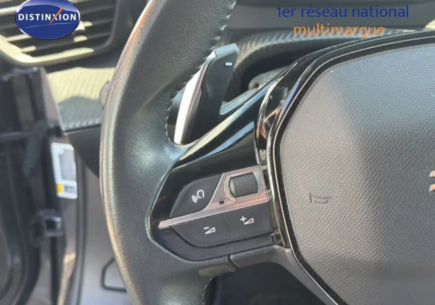 Gros plan sur le volant noir de la Peugeot 2008 1.2 PureTech 130, montrant les commandes audio et la palette de changement de vitesse.