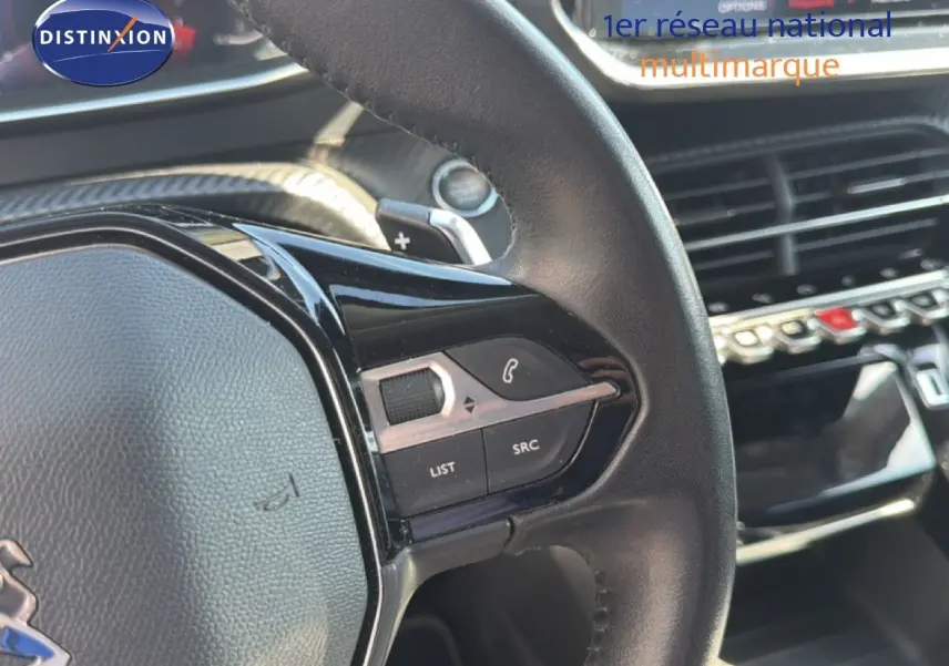 Gros plan sur le volant cuir noir de la Peugeot 2008 1.2 PureTech 130 Allure avec commandes intégrées et tableau de bord moderne.