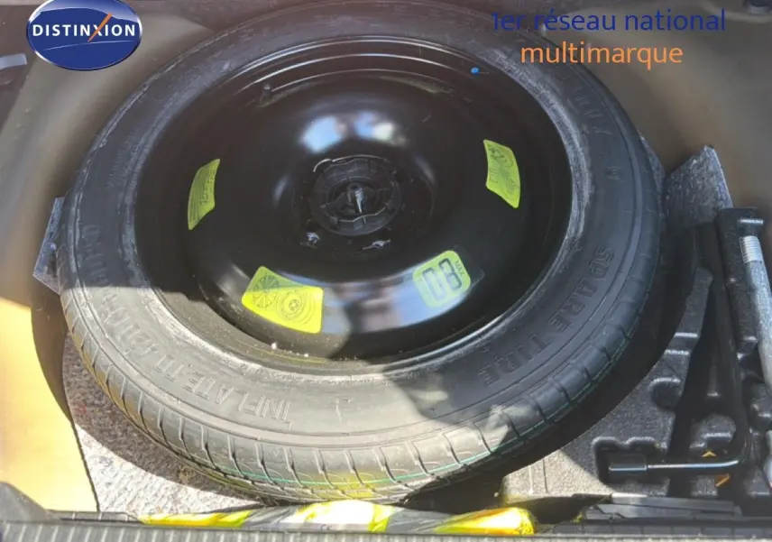 Vue plongeante sur la roue de secours noire et ses outils dans le coffre d'une Peugeot 2008 gris platinium.