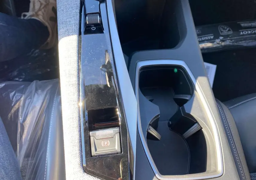 Gros plan sur la console centrale du Peugeot 3008 noir 2025, avec frein de stationnement électrique et porte-gobelets.