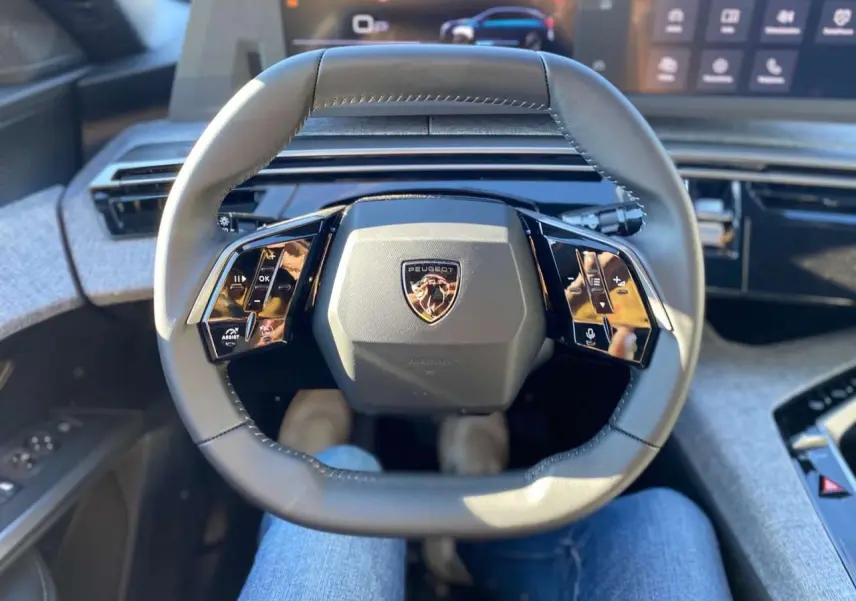 Vue intérieure centrée sur le volant cuir noir du Peugeot 3008 2025 avec commandes tactiles et logo au centre.