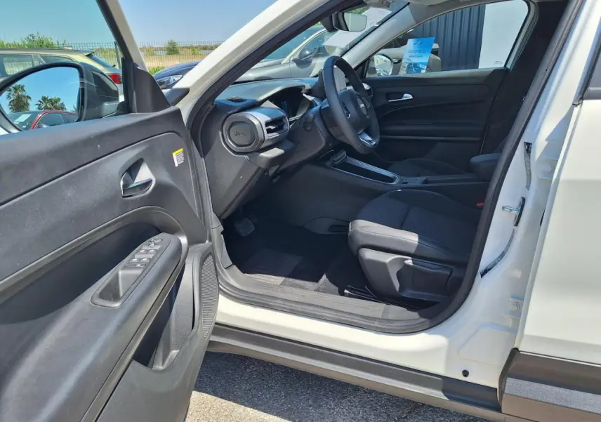 Intérieur côté conducteur du Jeep Avenger électrique blanc 2025, avec tableau de bord et sièges noirs visibles.