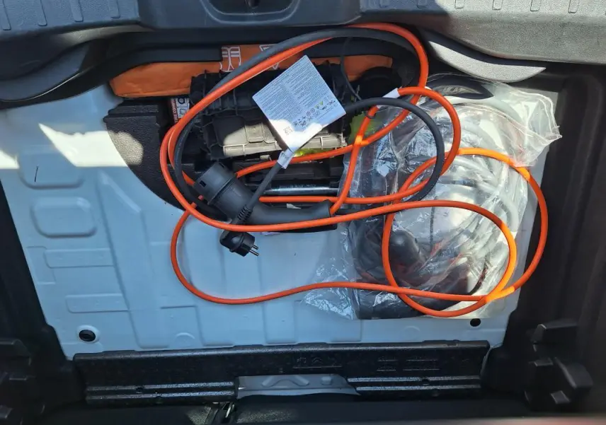 Vue du coffre ouvert d'un Jeep Avenger blanc 2025, montrant le câble de recharge électrique orange rangé.