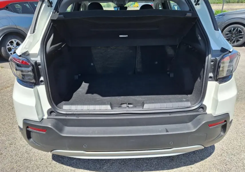 Vue arrière du coffre ouvert d'une Jeep Avenger électrique blanche, avec feux arrière et pare-chocs visibles.