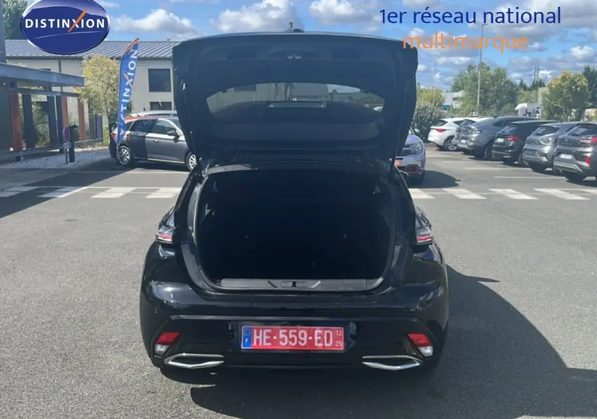 Vue arrière d'une Peugeot 308 noir métal 2025 avec coffre ouvert, stationnée sur un parking en extérieur.