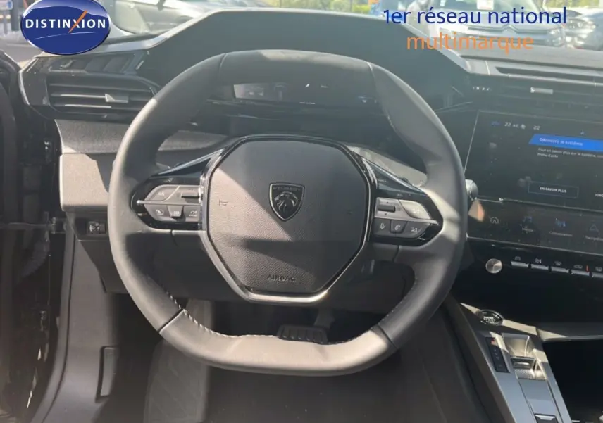 Vue intérieure centrée sur le volant noir de la Peugeot 308 Hybrid 145ch 2025 avec tableau de bord et console tactile visibles.
