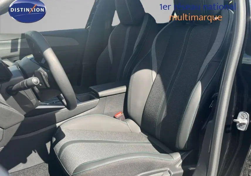 Vue intérieure côté conducteur de la Peugeot 308 Hybrid 2025, siège bi-matière gris noir avec surpiqûres vertes.