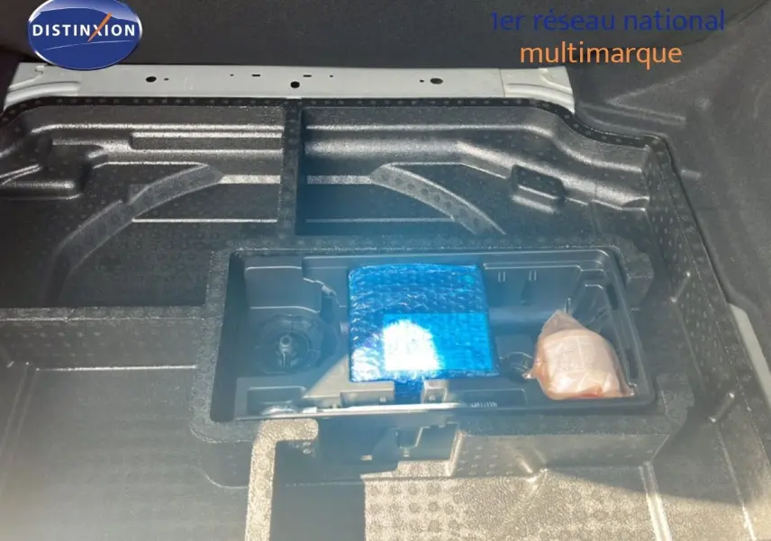 Coffre ouvert de la Peugeot 308 noir métal, vue plongeante sur le rangement sous plancher avec accessoires emballés.