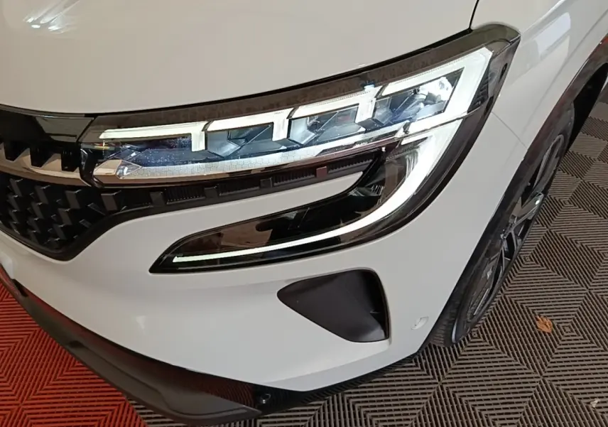 Gros plan sur le phare avant droit blanc du Renault Austral Techno E-Tech Hybride 200 avec calandre noire et jante visible.