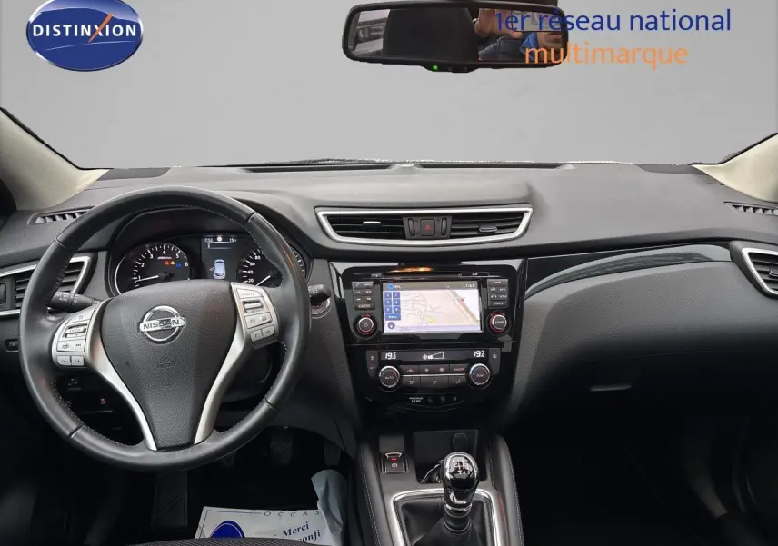 Vue intérieure frontale du Nissan Qashqai blanc glacier 2017, mettant en valeur le volant, la console centrale avec écran tactile et la boîte manuelle.