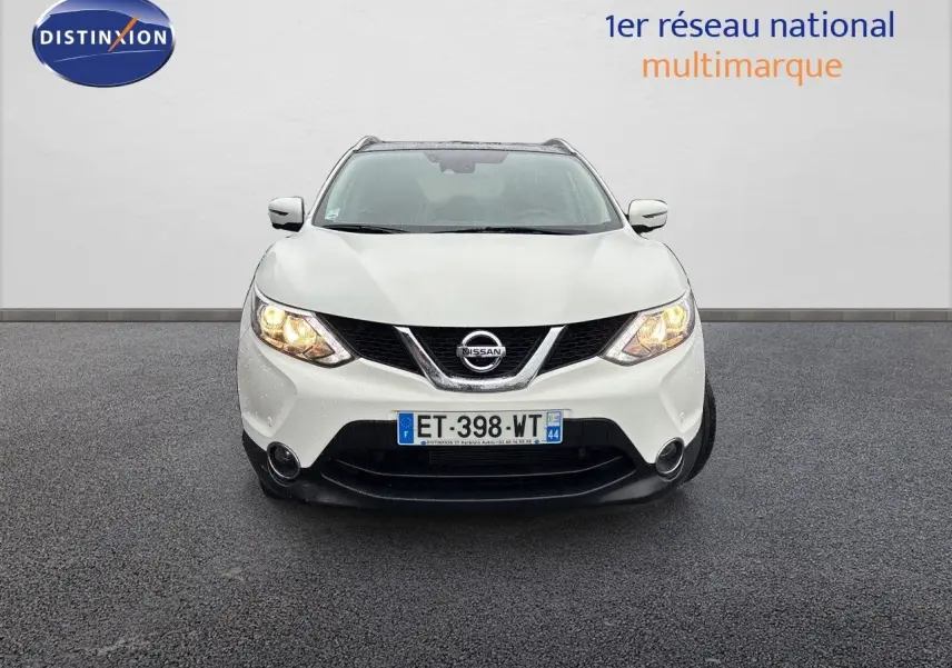 Vue frontale d'un Nissan Qashqai blanc glacier de 2017 avec phares allumés sur sol gris.