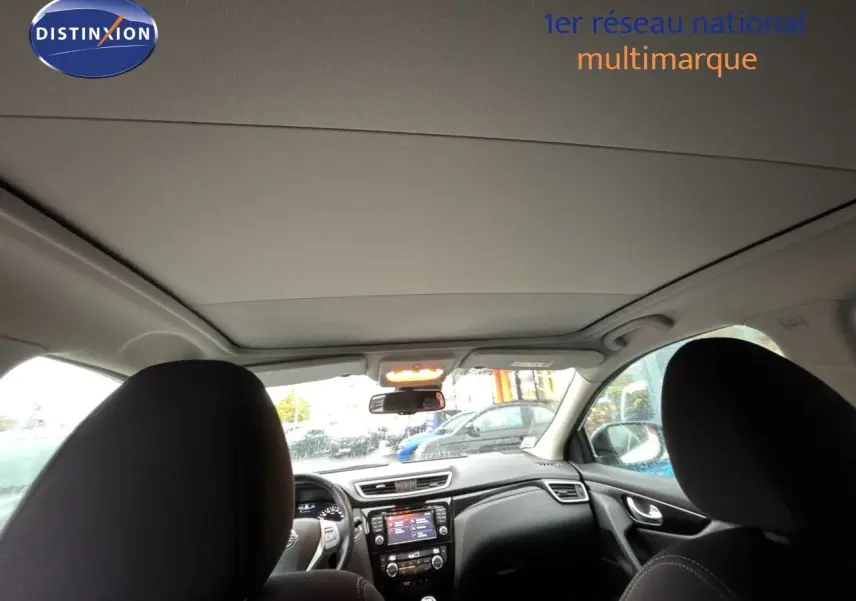 Vue intérieure du Nissan Qashqai blanc glacier 2017, montrant le tableau de bord et les sièges avant en tissu noir.