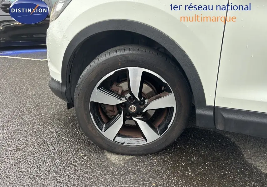 Gros plan sur la roue avant droite du Nissan Qashqai blanc glacier, avec jante alliage bi-ton distincte.