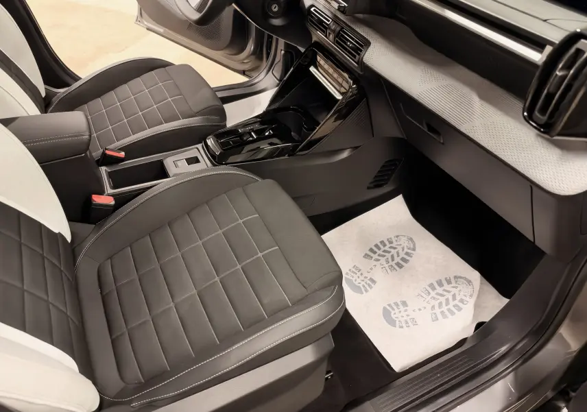Vue intérieure côté passager de la Citroën E-C3 2025 gris, sièges noirs avec surpiqûres blanches et console centrale brillante.