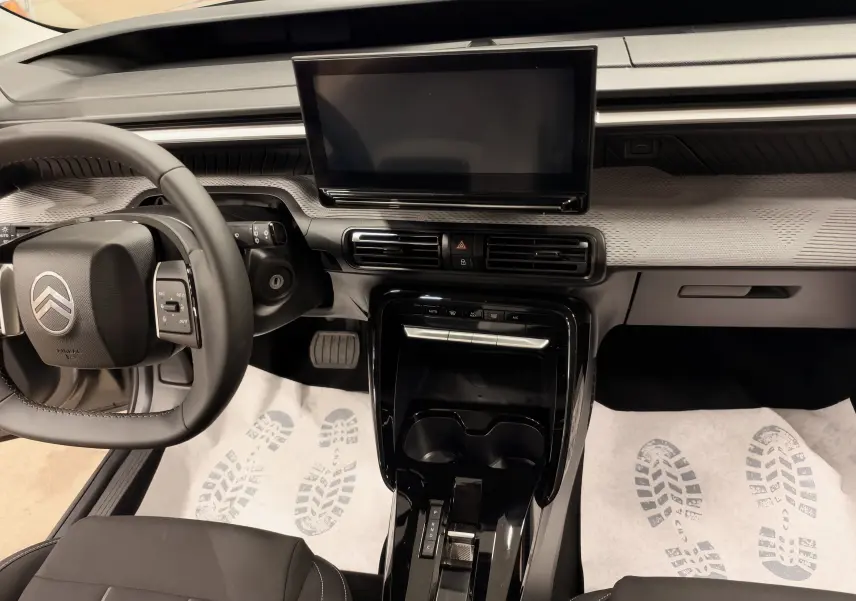 Vue intérieure de face du tableau de bord et console centrale noire de la Citroën E-C3 2025 gris, avec écran tactile et volant multifonction.
