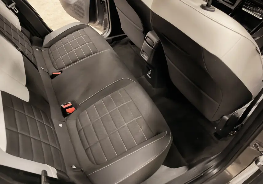 Vue intérieure arrière droite de la Citroën E-C3 2025, sièges noirs avec surpiqûres blanches et porte ouverte.