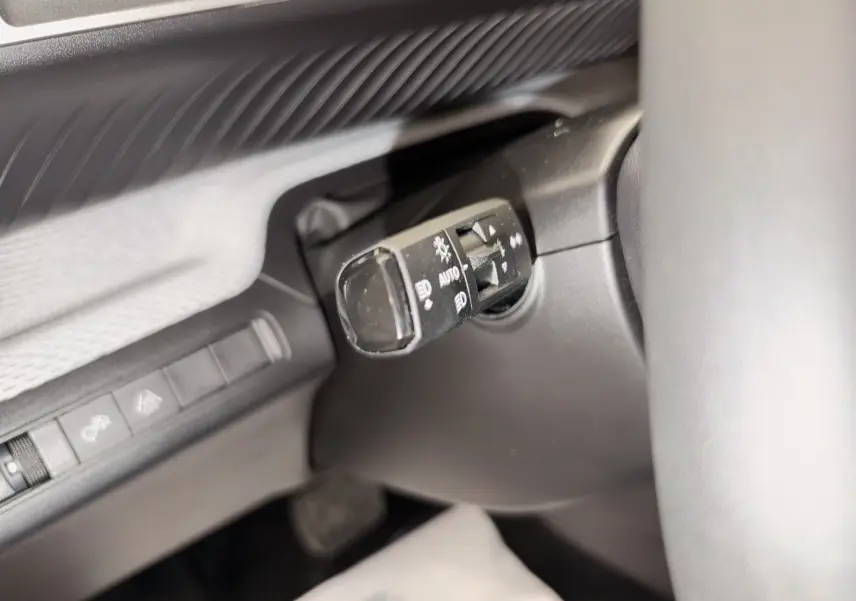 Gros plan sur la commande des phares à gauche du volant dans l’habitacle noir d’une Citroën C3 électrique gris.
