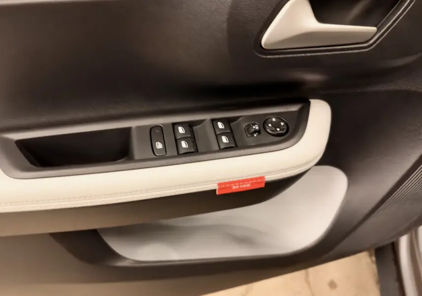 Gros plan sur la commande des vitres et rétroviseurs côté conducteur de la porte intérieure noire et beige d'une Citroën C3 gris 2025.