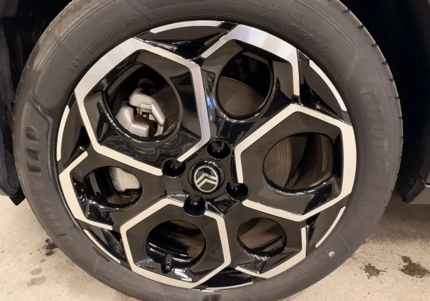 Gros plan sur la jante noire et argentée d’une Citroën E-C3 gris 2025, mettant en valeur le logo central et le pneu Goodyear.