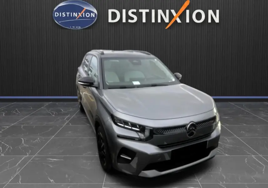 Citroën E-C3 gris en 3/4 avant droit, avec calandre noire et phares LED, sur fond intérieur showroom Distinxion.