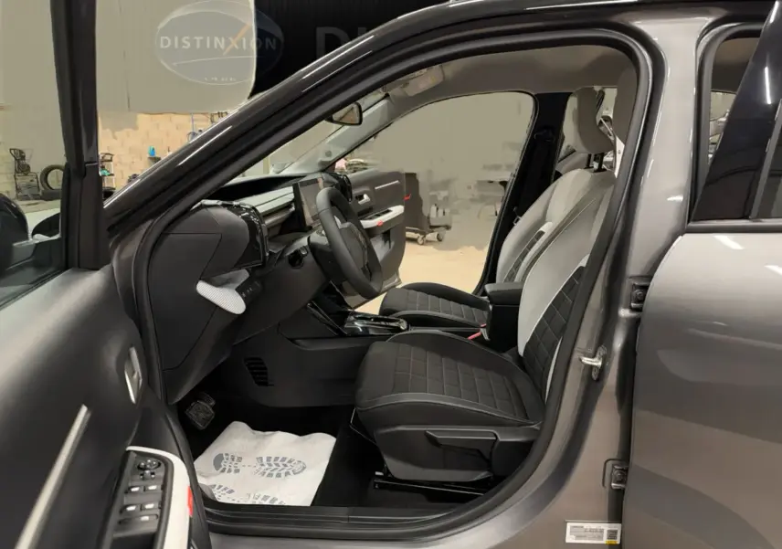 Vue intérieure côté conducteur d'une Citroën E-C3 gris 2025, sièges bi-ton noir et clair avec volant et tableau de bord modernes.