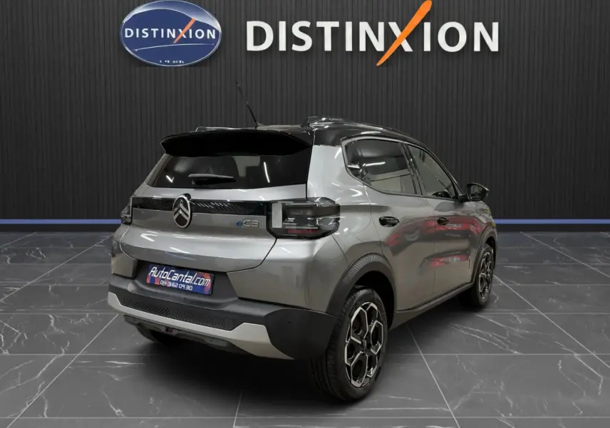 Vue 3/4 arrière droite d'une Citroën E-C3 électrique gris métallisé avec toit noir et jantes bi-ton en showroom.