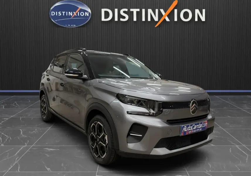 Citroën E-C3 gris en 3/4 avant droit, avec jantes bi-ton et calandre épurée, sur fond intérieur showroom.