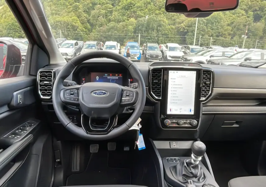 Vue intérieure centrée sur le tableau de bord et volant du Ford Ranger rouge racing 2025 avec boîte manuelle.
