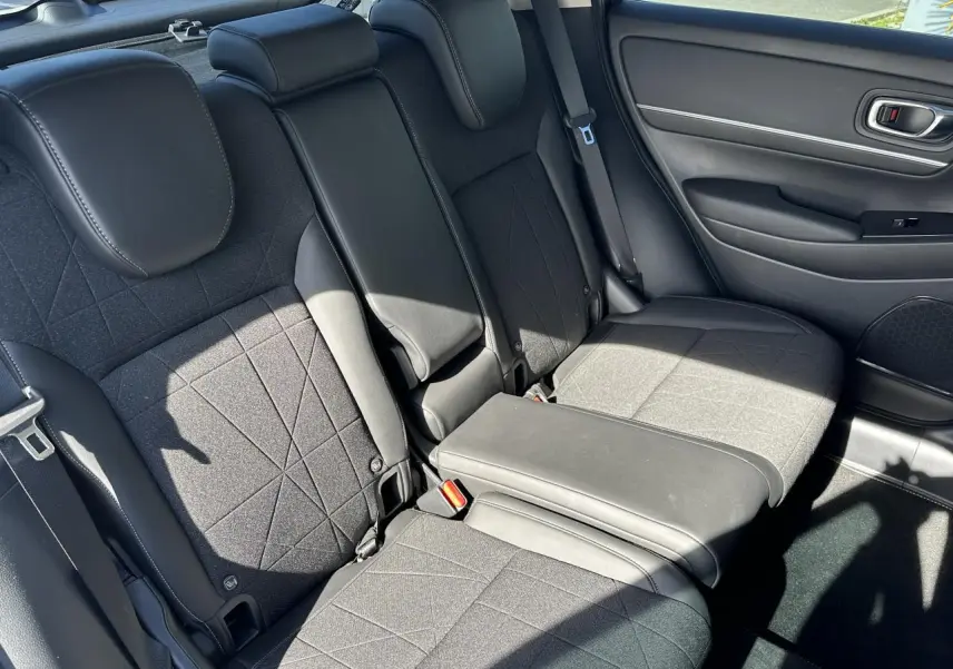 Vue intérieure arrière droite du Honda HR-V 2025 gris, montrant les sièges arrière en tissu et cuir synthétique noirs avec accoudoir central abaissé.