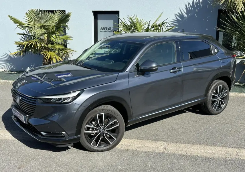 Honda HR-V gris métallisé vu de 3/4 avant droit, avec jantes alliage noires et détails modernes sur carrosserie.