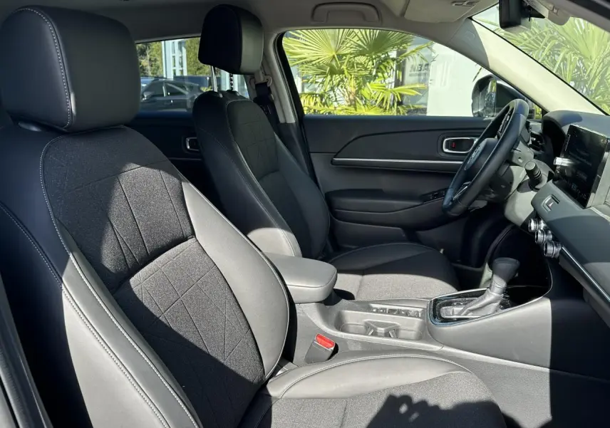 Intérieur avant du Honda HR-V 2025, sièges cuir synthétique et tissu noirs, console centrale avec levier de boîte automatique.
