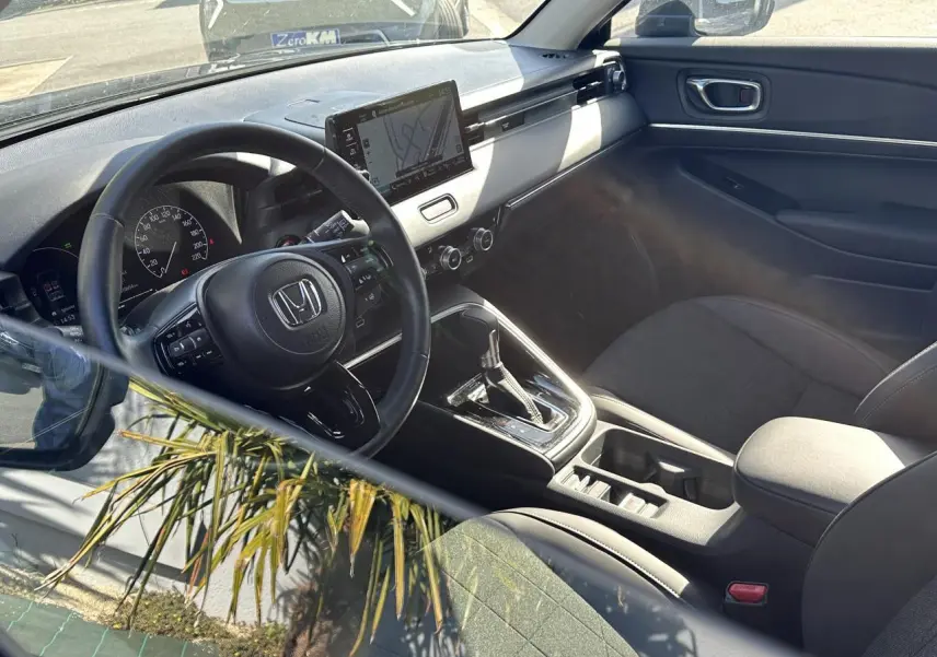 Intérieur du Honda HR-V 2025 vu côté conducteur, volant cuir, écran tactile central et sièges noirs en tissu et cuir.