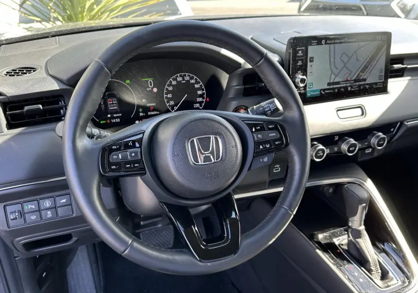 Vue intérieure centrée sur le volant cuir noir et le tableau de bord digital du Honda HR-V 2025 gris hybride.