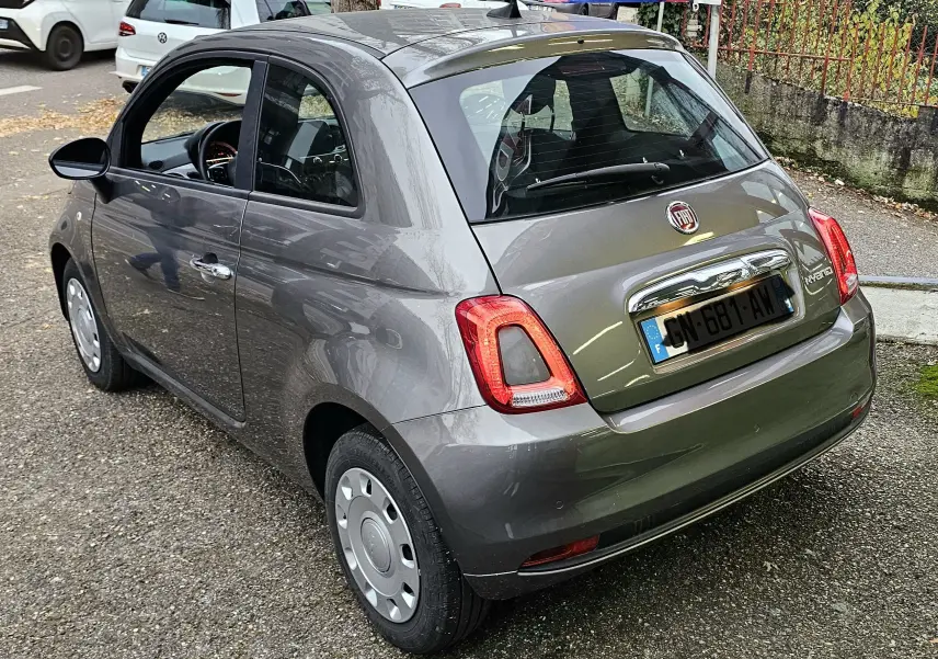 Vue 3/4 arrière gauche d'une FIAT 500 gris métallisé 2023 avec feux arrière caractéristiques et jantes acier.