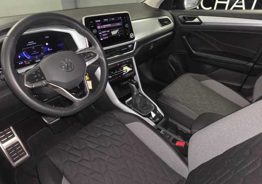 Intérieur avant du Volkswagen T-Roc 2025, sièges tissu noir/gris, tableau de bord gris étain avec écran tactile 8 pouces.