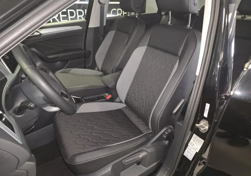 Vue intérieure côté conducteur du Volkswagen T-Roc noir, mettant en valeur les sièges tissu noir et gris avec coutures apparentes.