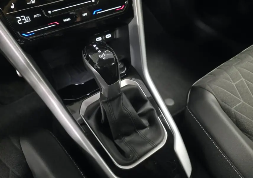 Gros plan sur la console centrale noire du Volkswagen T-Roc 2025 avec levier de vitesse automatique et sièges tissu gris.