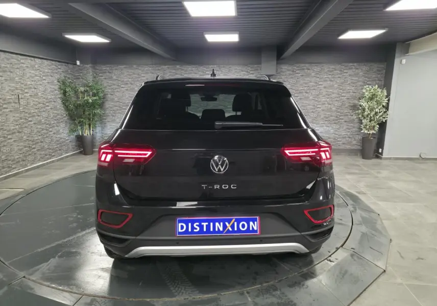 Vue arrière d'un Volkswagen T-Roc noir 2025 avec feux LED allumés dans un showroom intérieur.