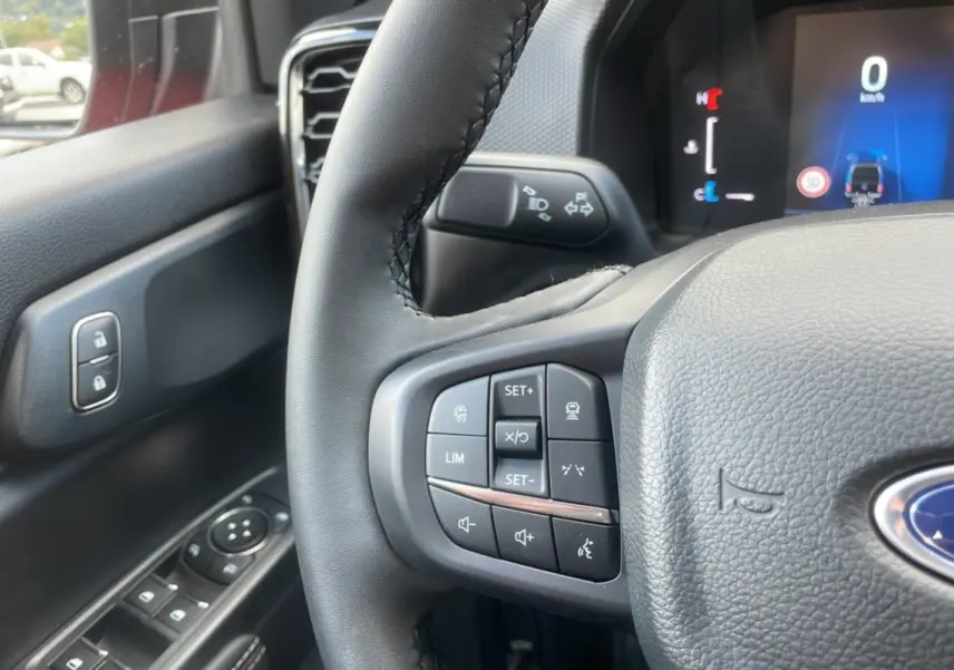 Gros plan sur le volant du Ford Ranger 2025 rouge racing, montrant les commandes multifonctions côté gauche et tableau de bord numérique.