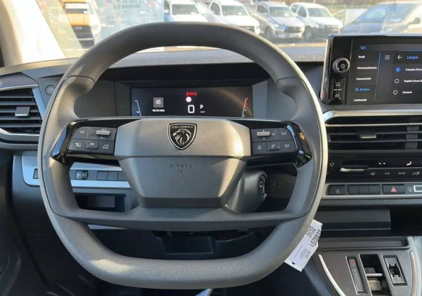 Vue intérieure centrée sur le volant multifonctions et les écrans digitaux du Peugeot Traveller gris acier 2025.