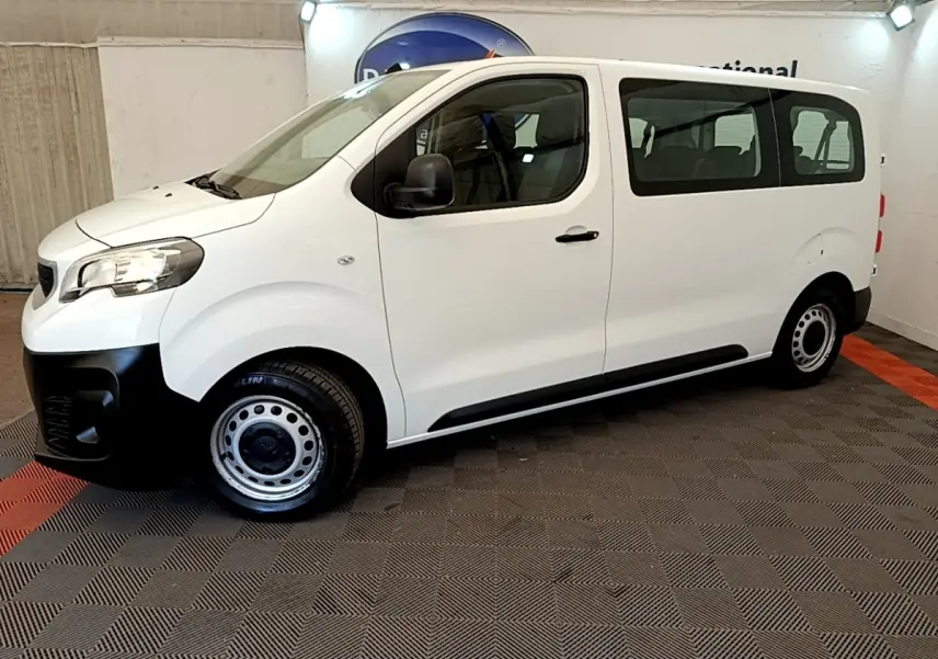 Vue de profil côté gauche d’un Peugeot Traveller blanc 2018 avec jantes acier et pare-chocs noirs, en intérieur.