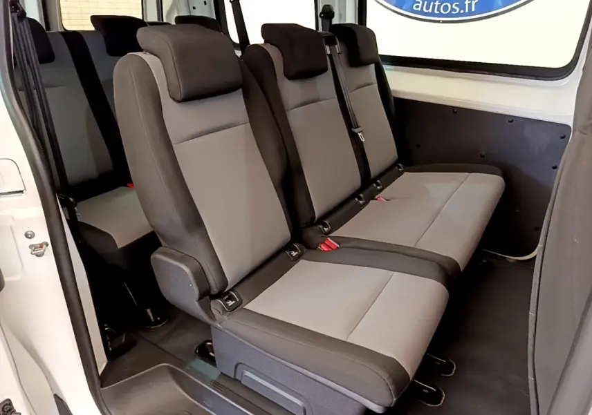 Vue intérieure latérale droite des sièges gris et noirs du Peugeot Traveller blanc de 2018 avec porte coulissante ouverte.
