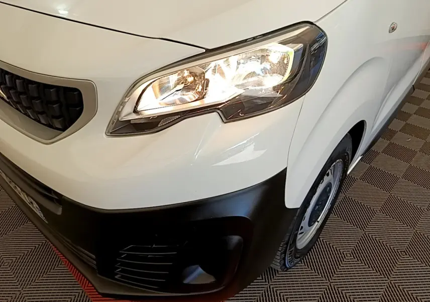 Gros plan sur l’avant droit du Peugeot Traveller blanc de 2018, avec phare allumé et pare-chocs noir mat.
