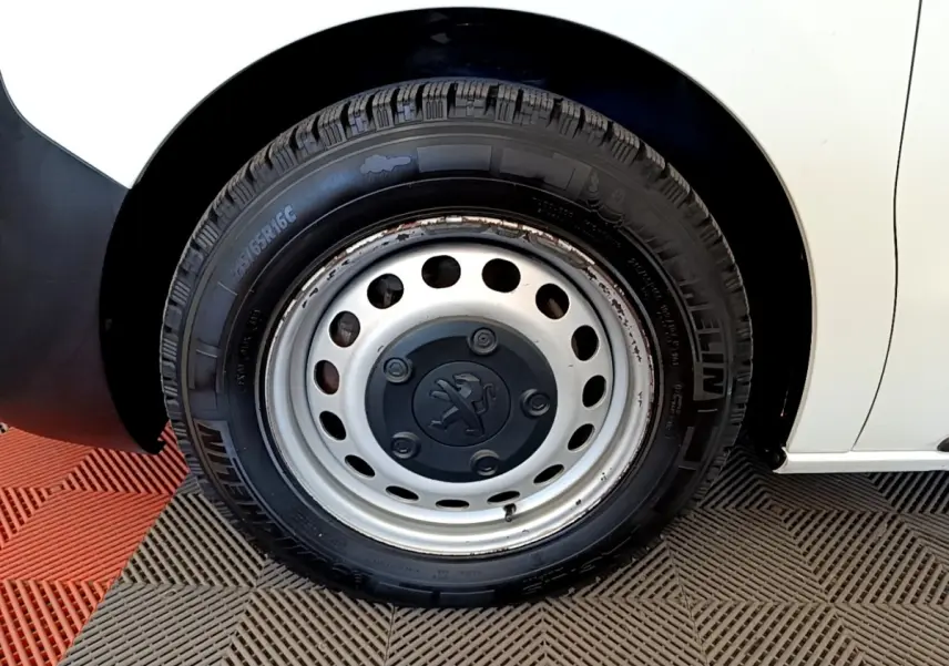 Gros plan sur la roue avant gauche d’un Peugeot Traveller blanc de 2018 avec jante acier et logo Peugeot central.