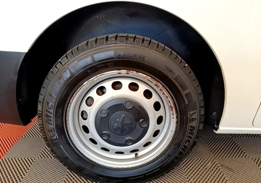 Gros plan sur la roue arrière droite d’un Peugeot Traveller blanc de 2018, avec jante acier et traces de rouille.